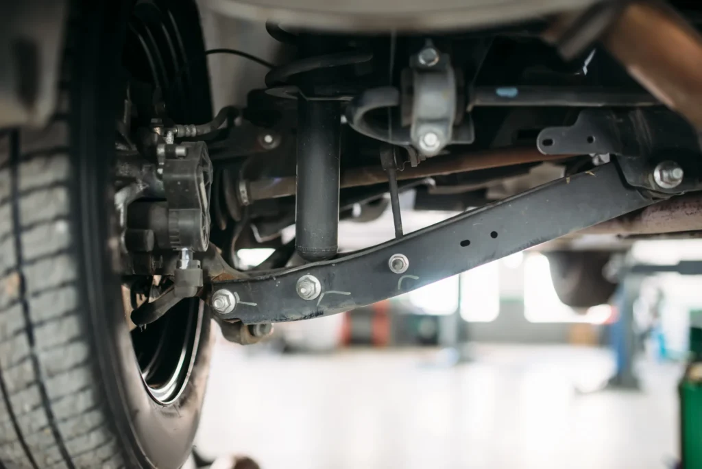 Detalhe do sistema de suspensão automotiva com amortecedor, braço de suspensão e componentes da roda em inspeção mecânica.