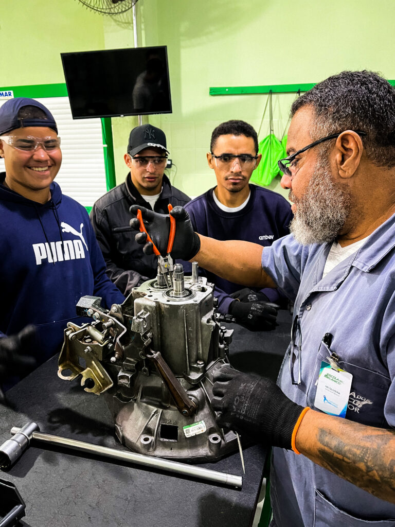 Instrutor técnico orientando alunos em aula prática de mecânica automotiva na Escola do Mecânico.