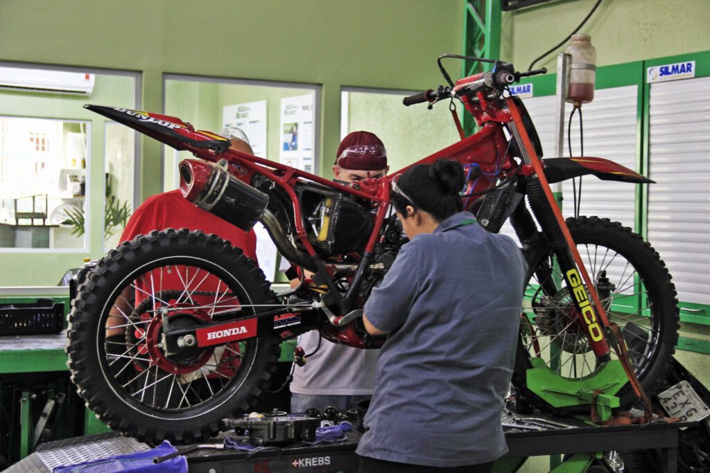 Mecânico profissional realizando o ajuste e a lubrificação da corrente de transmissão de uma motocicleta em cavalete.