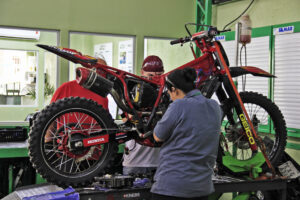 Mecânico profissional realizando o ajuste e a lubrificação da corrente de transmissão de uma motocicleta em cavalete.