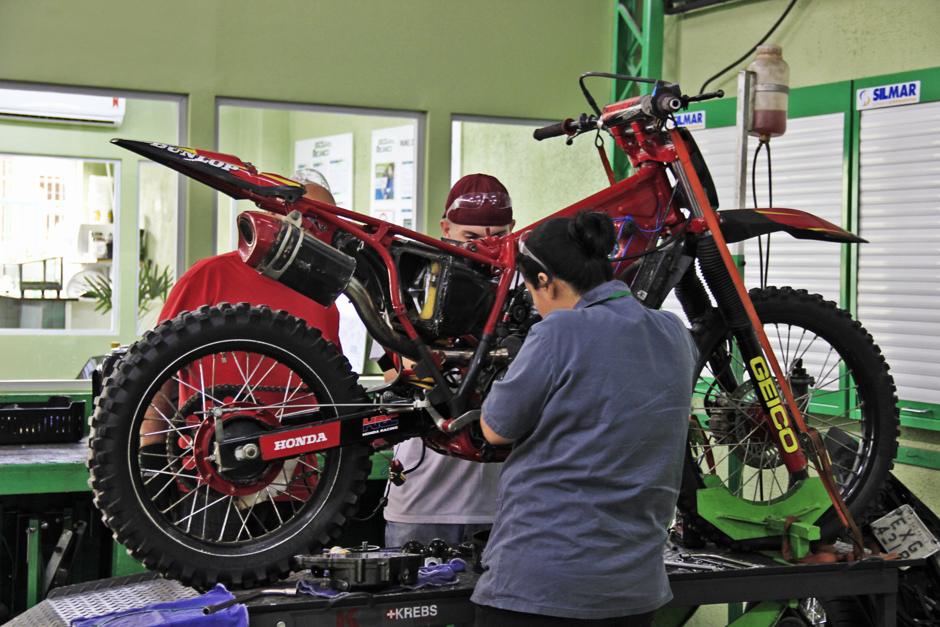 Mecânico profissional realizando o ajuste e a lubrificação da corrente de transmissão de uma motocicleta em cavalete.