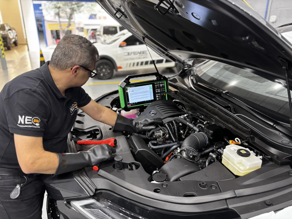 Mecânico automotivo com luvas de proteção isolantes realizando o diagnóstico de carro híbrido e elétrico conectado a equipamentos de leitura técnica na oficina.