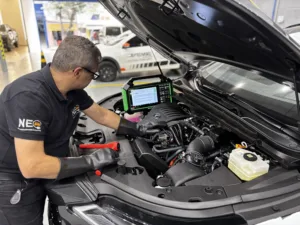 Mecânico automotivo com luvas de proteção isolantes realizando o diagnóstico de carro híbrido e elétrico conectado a equipamentos de leitura técnica na oficina.