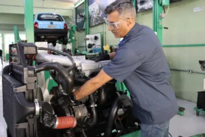 Mecânico profissional realizando o diagnóstico técnico e a manutenção de um motor diesel de grande porte com ferramentas especializadas em uma oficina de linha pesada.